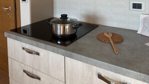 Una cocina moderna con armarios de madera clara, una cocina por inducción negra y una olla de acero inoxidable.