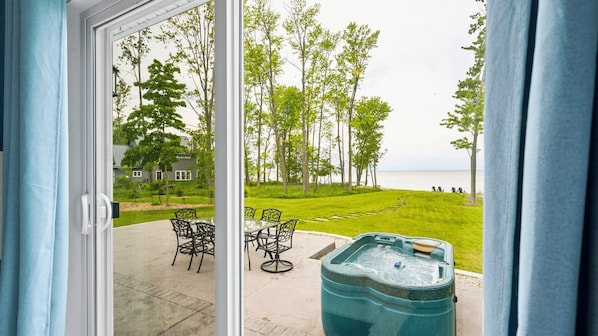 A patio with a hot tub, outdoor furniture, and a view of a grassy area with trees and a body of water.