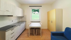 Cocina compacta con una mesa de comedor y sillas, una ventana con vistas a follaje, y una silla azul.
