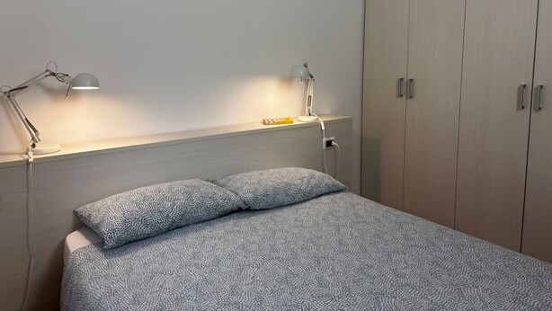 Un dormitorio con una cama, dos lámparas de noche, una mesita de noche y un armario.
