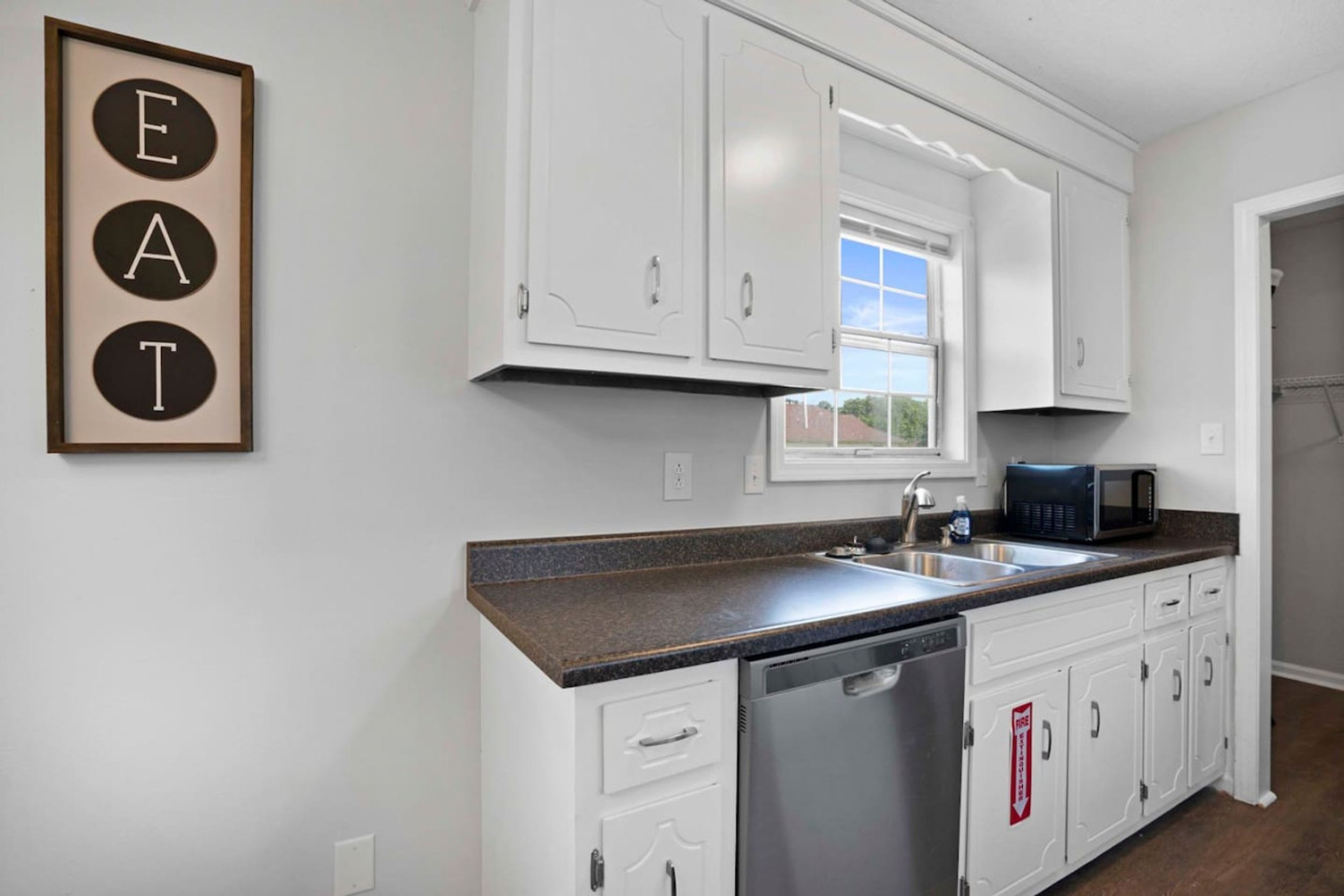 A kitchen with white cabinets, a granite countertop, a dishwasher, a microwave, and a window with a view.