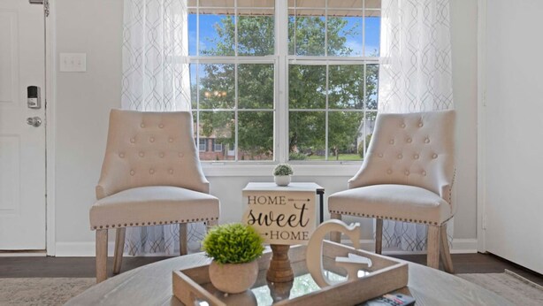 A room with two upholstered chairs, a small table with a tray, a sign reading 'HOME sweet HOME', and a view through a window. - Charming House Close to Fort Campbell and Casino (Clarksville)