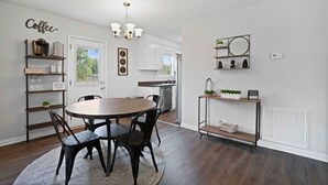 A dining area with a round table, chairs, a chandelier, a coffee-themed wall, and a kitchen in the background. - Charming House Close to Fort Campbell and Casino (Clarksville)