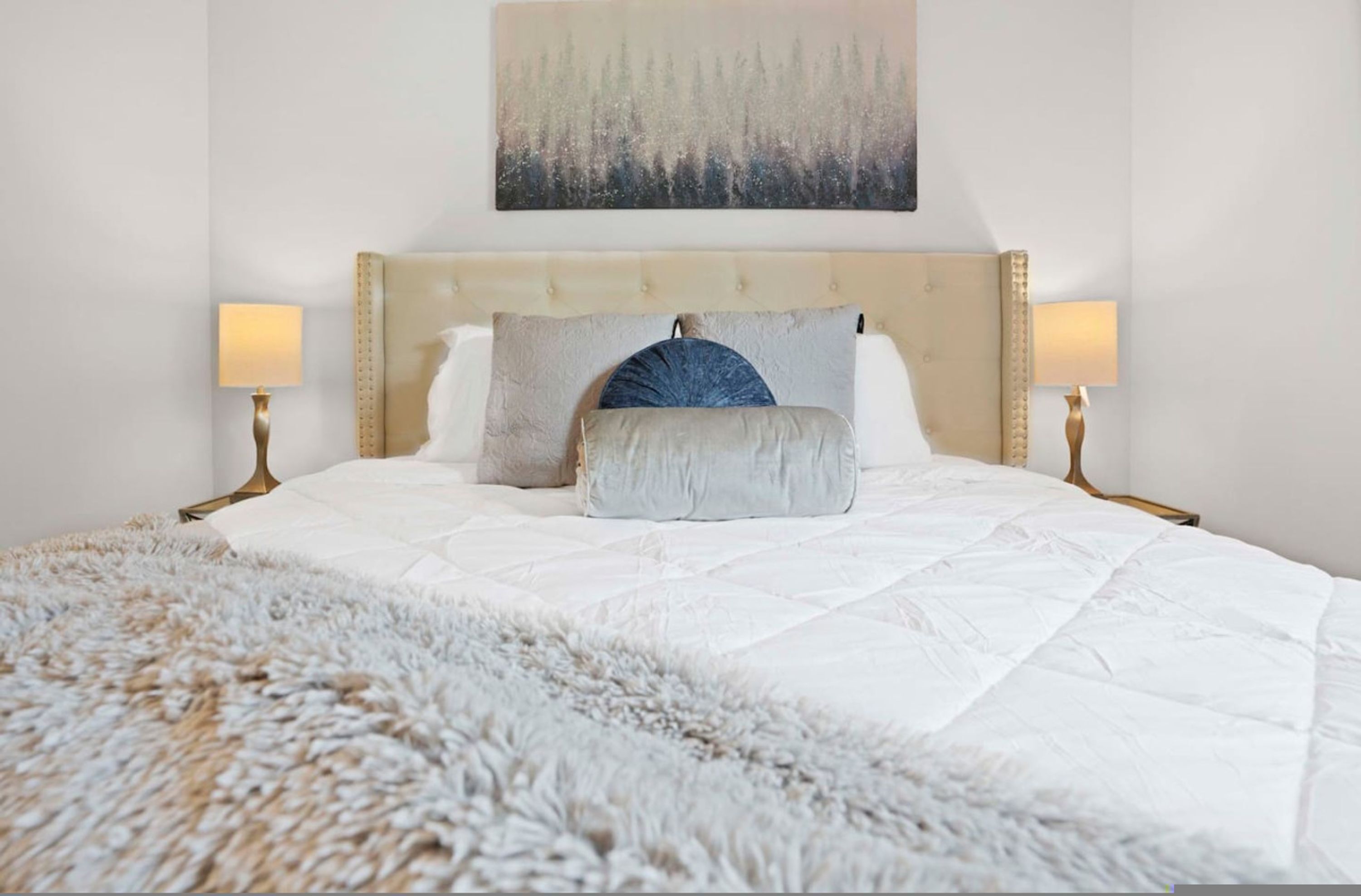 A bed with a tufted headboard, two bedside lamps, and a fluffy rug.
