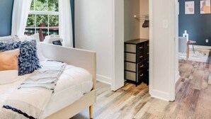 A bedroom with a bed, a ceiling fan, a window with white curtains, and a wooden floor. - Cozy Oasis of Downtown Clarksville (Clarksville)