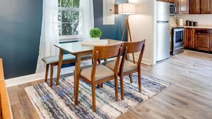 A dining area with a table and chairs, a window with curtains, a ceiling fan, and a kitchen area with cabinets and appliances. - Cozy Oasis of Downtown Clarksville (Clarksville)