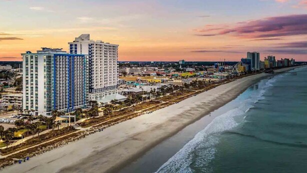 Un paysage urbain côtier avec un hôtel imposant, doté de nombreux étages et balcons, une large plage et une vue dégagée sur l’océan.