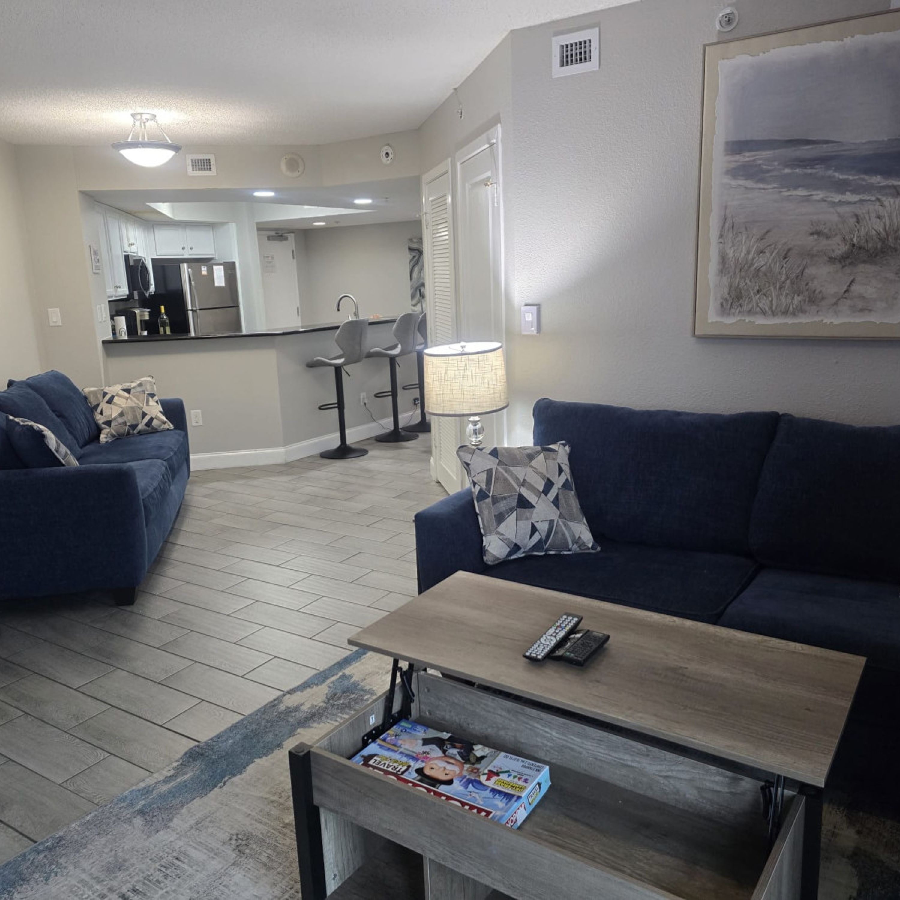 A living room with a blue sofa, a coffee table with magazines, and a kitchen in the background.