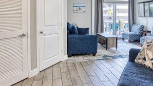 Un salon moderne avec un canapé bleu, une table basse et un téléviseur. On peut voir deux portes et un balcon.