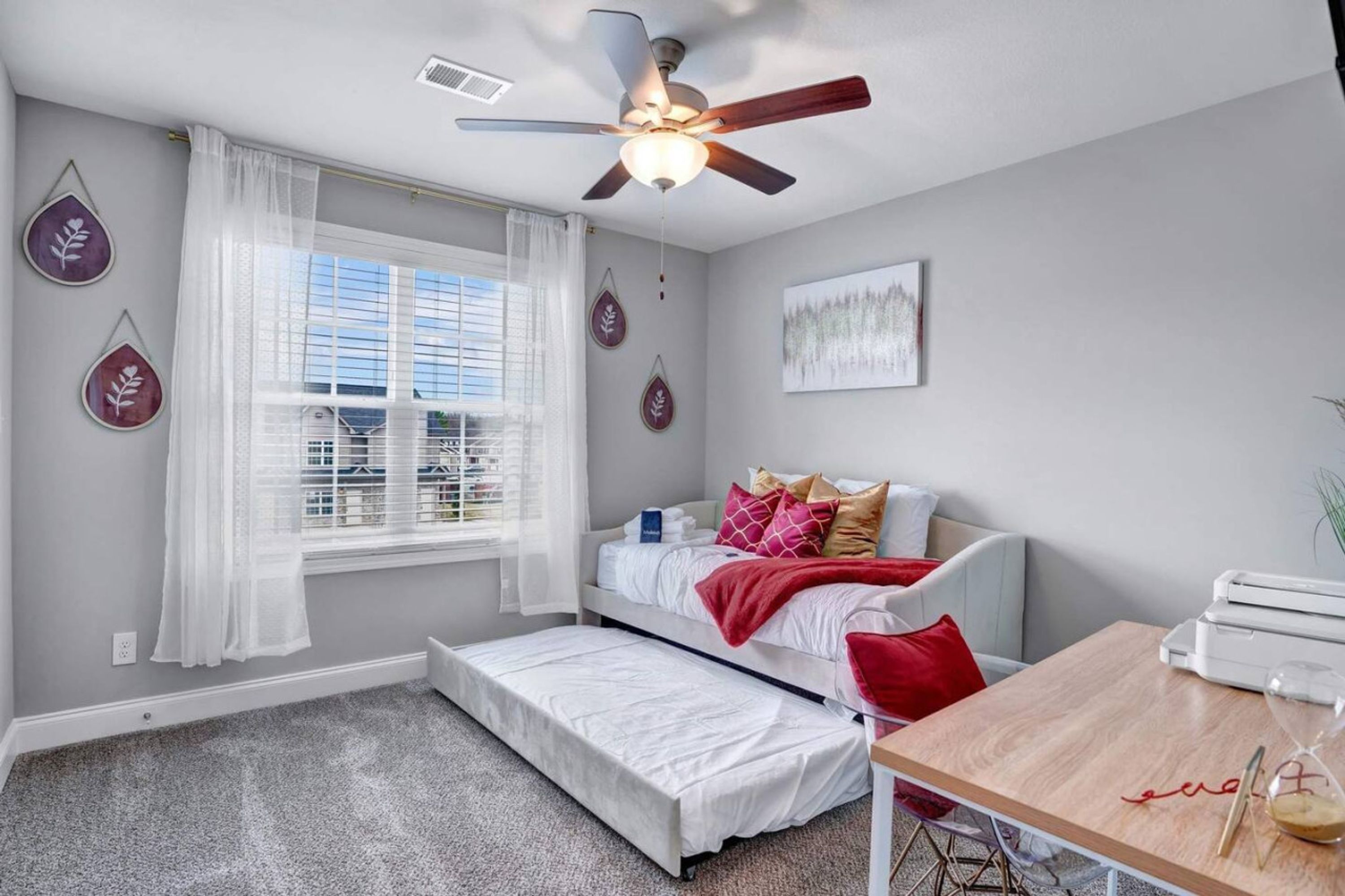 A bedroom with a bed, a desk, a ceiling fan, and a window with curtains.