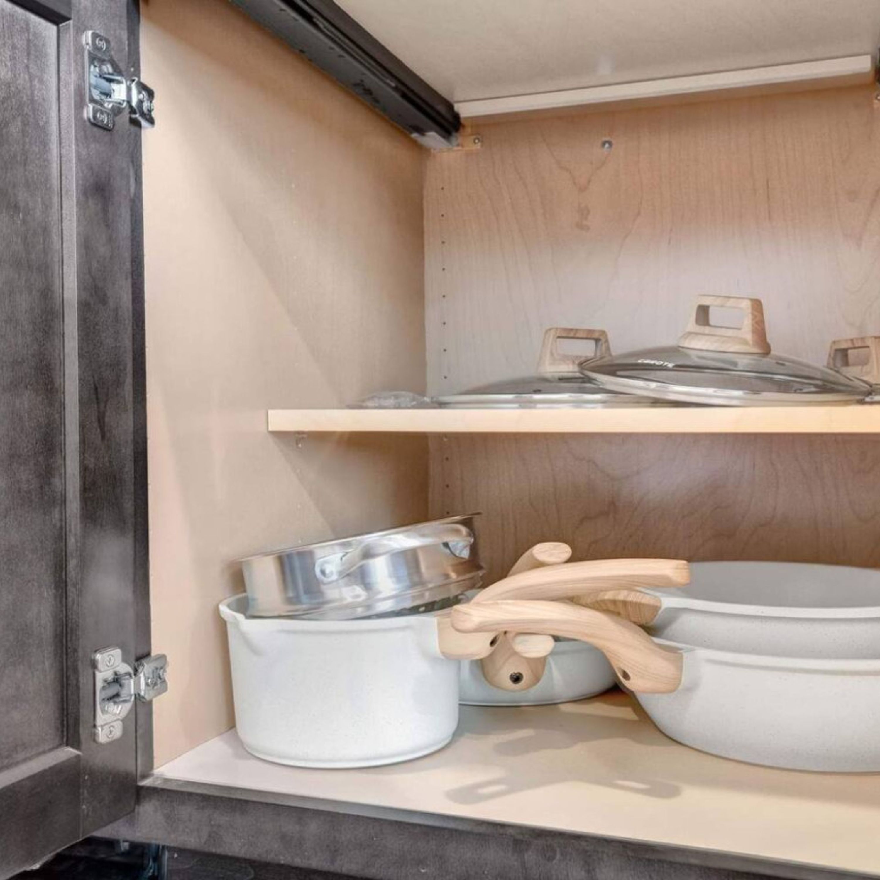 A kitchen cabinet with a wooden shelf and a lower shelf holding pots and pans.
