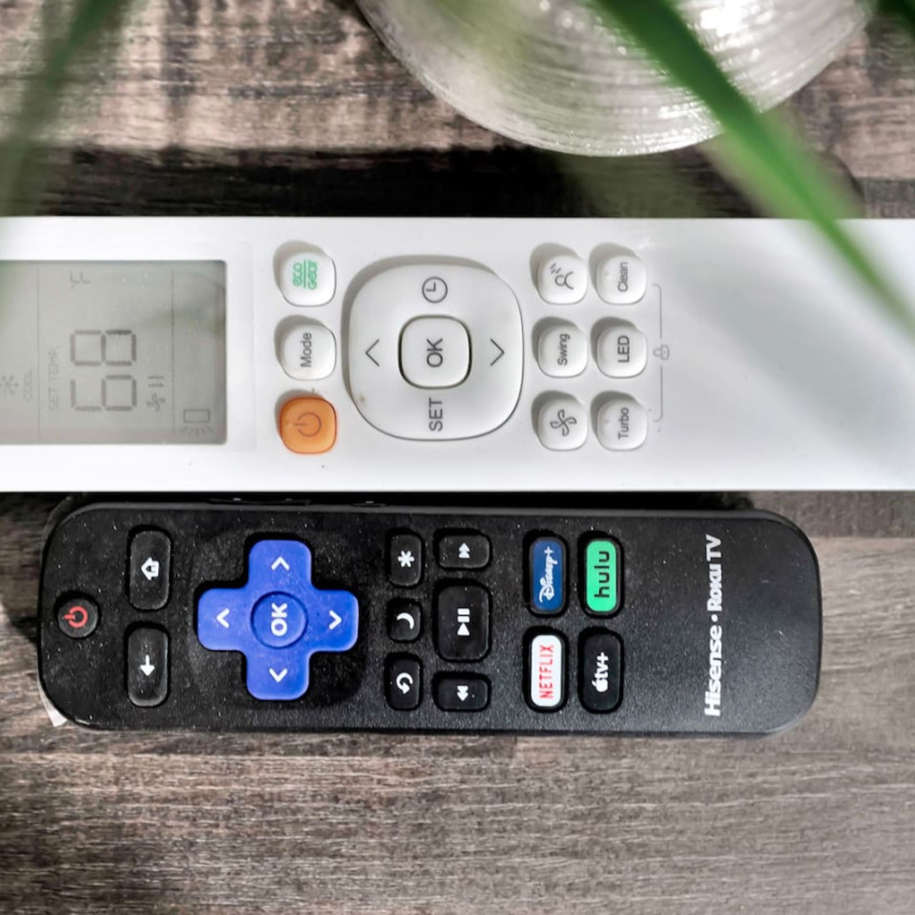 A white remote control with a digital display and various buttons including a blue 'OK' button, a red power button, and a blue 'OK' button on a black remote control with a blue directional pad and buttons labeled 'Disney+', 'hulu', 'Netflix', and 'Hulu TV'.