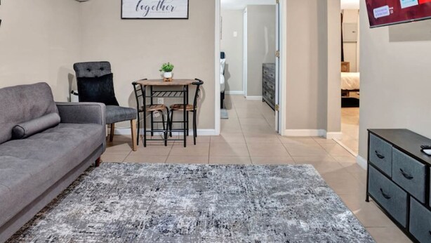 Een woonkamer met een grijze bank, een klein tafeltje met stoelen, een wandairconditioner en een bordje met de tekst 'Together'.