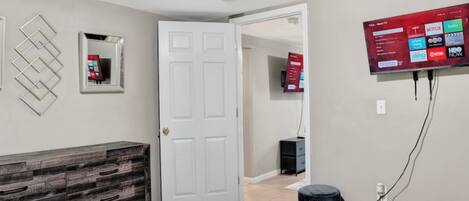 A bedroom with a bed, a dresser, a TV mounted on the wall, and a door leading to another room.
