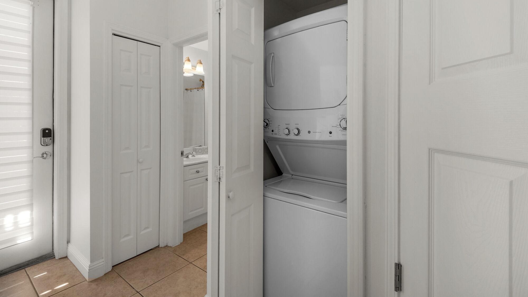 A laundry room with a front-loading washer and dryer, a sink, and a door leading to another room.