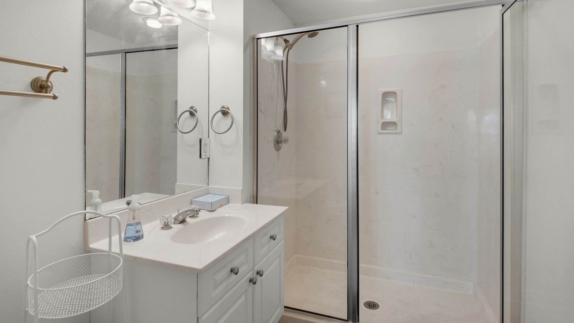 A modern bathroom with a glass shower enclosure, a white vanity with a mirror, and a metal shelf.
