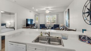 A modern hotel room with a large white kitchen area, a dining table, a sofa, and a TV. - Pool, Fitness Center & Central Location (Santa Rosa Beach)