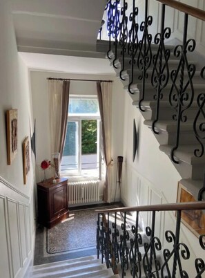 Stairs lead to an upper floor, flanked by white walls with decorative molding and a window with beige curtains.