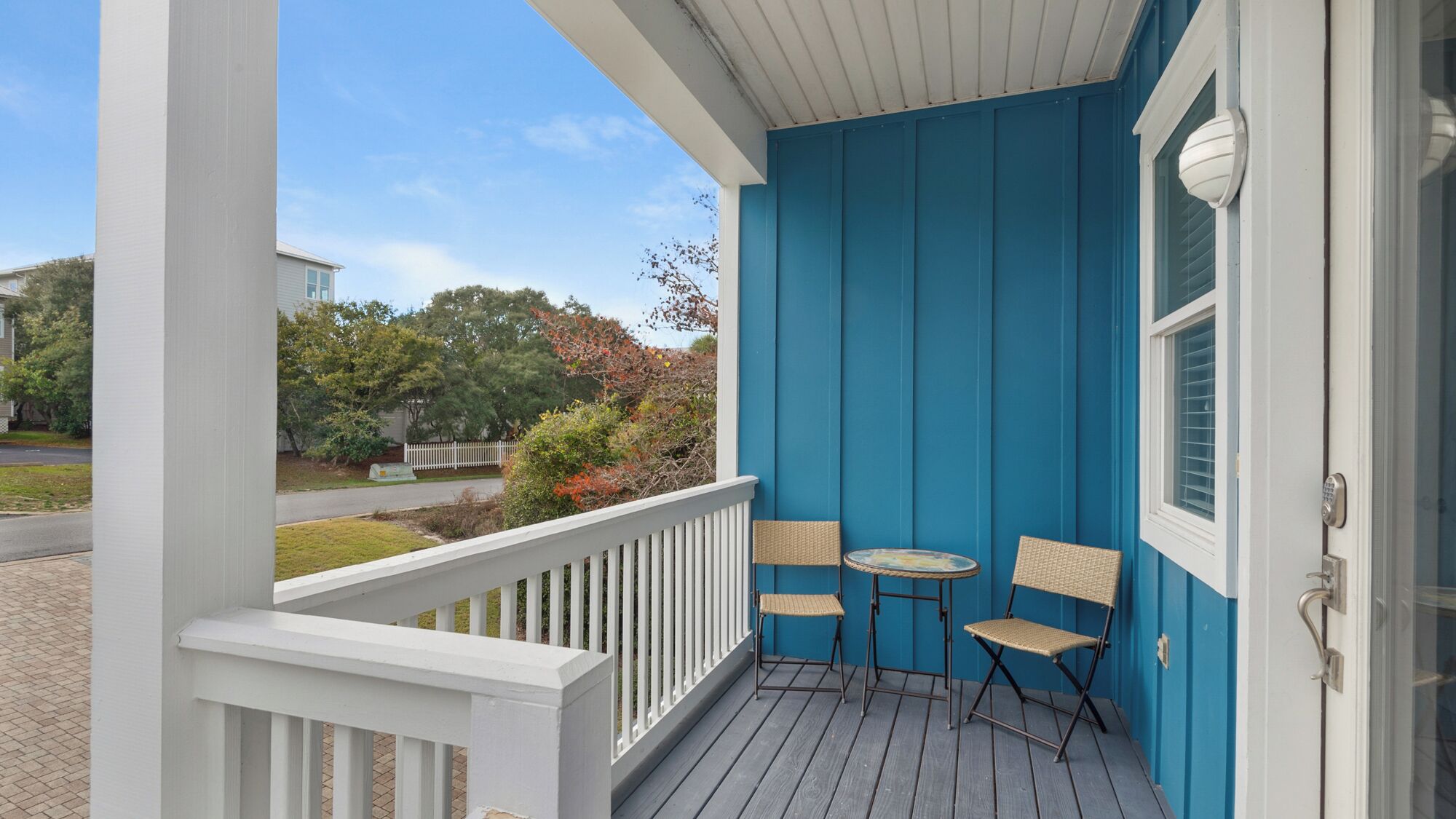 A blue porch with white railings, two wicker chairs, and a small round table.