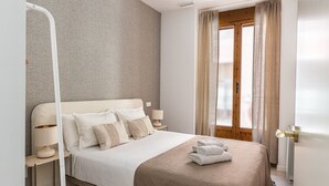 A bedroom with a bed, bedside lamps, a window with curtains, and a radiator.