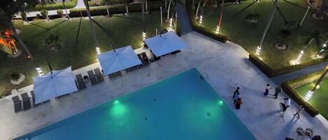 A swimming pool with lounge chairs and umbrellas, surrounded by well-manicured lawns and palm trees.