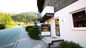 A restaurant with a signboard advertising a pizza menu, located in a mountainous area with a road in front.