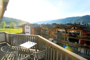 A balcony with a table and chairs, overlooking a mountainous landscape and a row of buildings. - Apartment Peter-Adler Resort (Kaprun)
