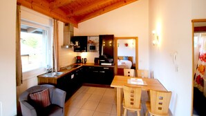 A compact kitchen with wooden cabinets, a dining area with a table and chairs, and a cozy seating area with a cushioned chair.