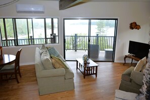 Relax in this spacious living room with a high ceiling, featuring a large sliding glass door leading to an outdoor deck with a natural view.