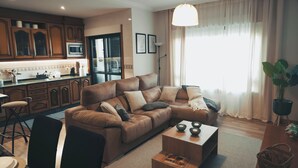 Een moderne woonkamer met een bruine leren bank, een houten salontafel, en een eethoek met een stoel en tafel.
