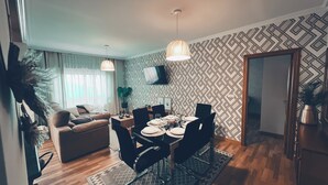 Een moderne woonkamer met een eethoek, met een bank, een aan de muur bevestigde televisie en behang met een patroon.