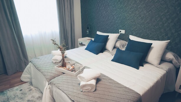 Een hotelkamer met een groot bed, twee kussens, een nachtkastje, een lamp en een dienblad met handdoeken en een klein vaasje.