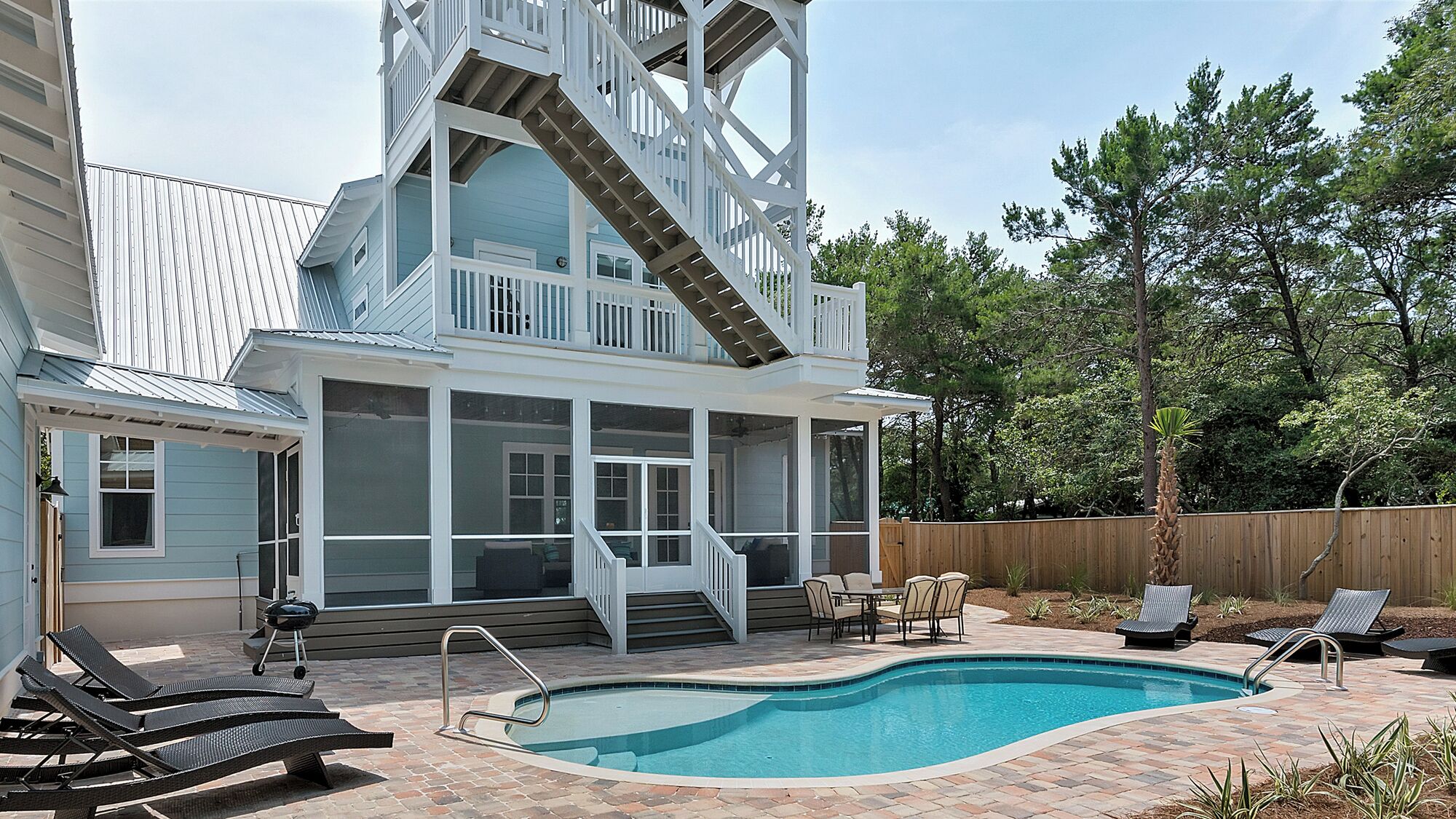 A two-story house with a large deck, a swimming pool, and outdoor furniture.