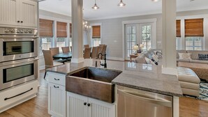 A modern kitchen with stainless steel appliances, a central island with a sink, and a dining area with wicker furniture. - Private Pool and Gulf Side in Seagrove + Beach Service (Santa Rosa Beach)