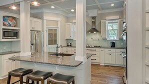 A modern kitchen with white cabinetry, a granite countertop, stainless steel appliances, and a central island with bar stools. - Private Pool and Gulf Side in Seagrove + Beach Service (Santa Rosa Beach)