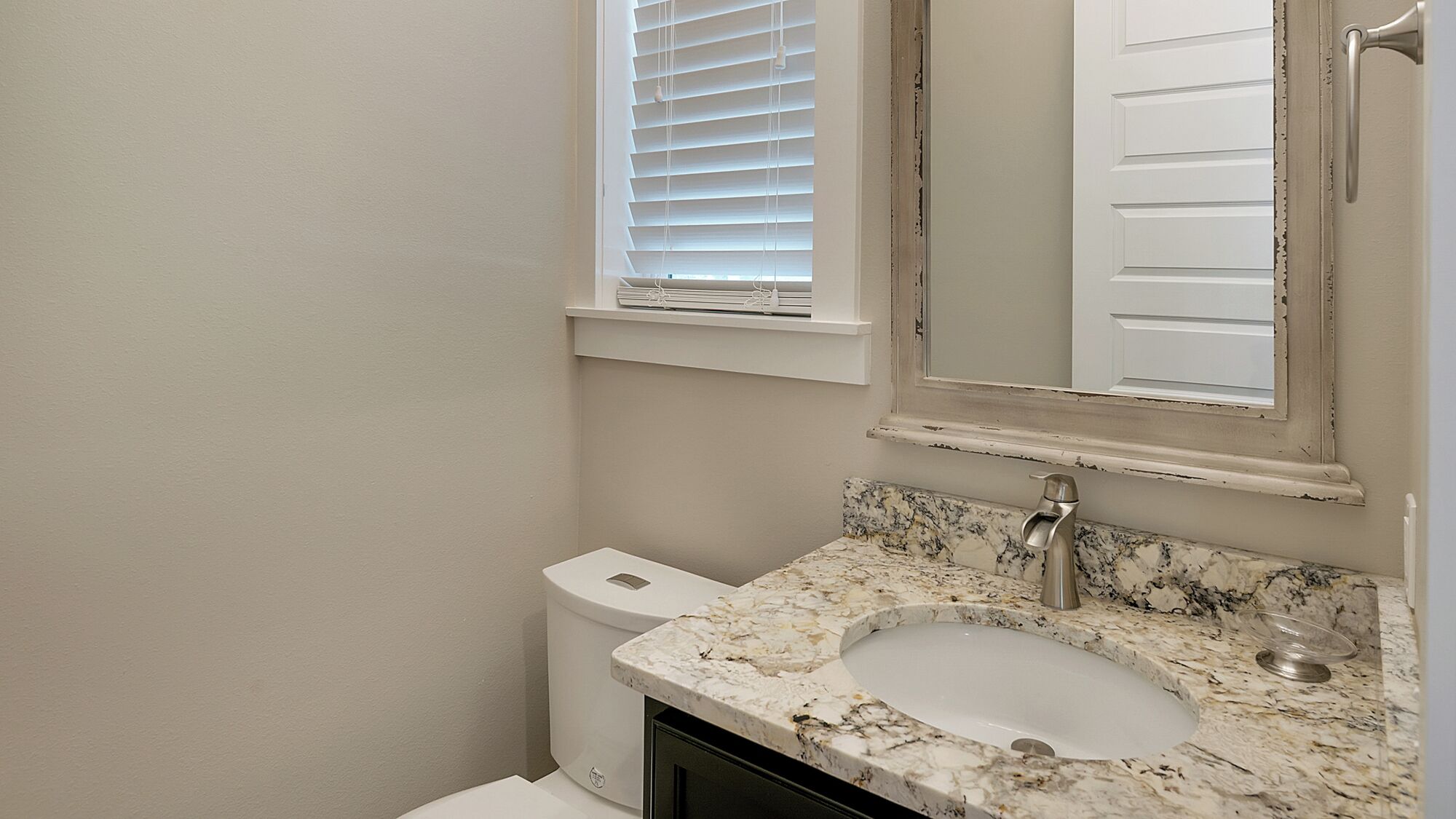 A bathroom with a white sink, a toilet, and a window with blinds.