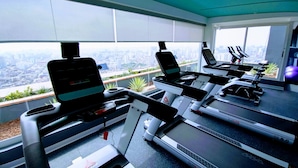 A gym with treadmills and elliptical machines, large windows with a city view, and exercise balls.