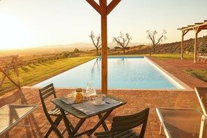 Ein Poolbereich mit Frühstückstisch, Blick auf den Pool und einer Pergola.