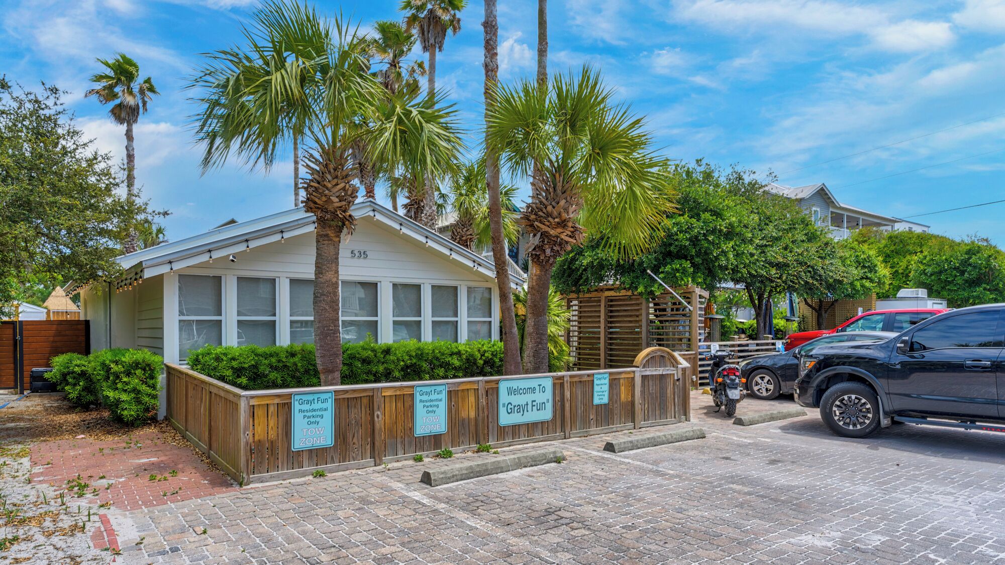 A residential building with a gated driveway, palm trees, and a brick pathway.