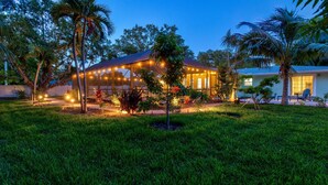A house with a covered patio area, surrounded by lush greenery and palm trees. - Luxury Getaway | Saltwater Pool, Fire Pit & Games! (Bradenton)