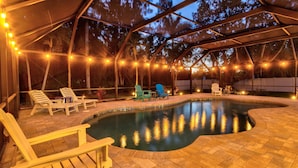 A covered outdoor swimming pool area with lounge chairs and string lights. - Luxury Getaway | Saltwater Pool, Fire Pit & Games! (Bradenton)