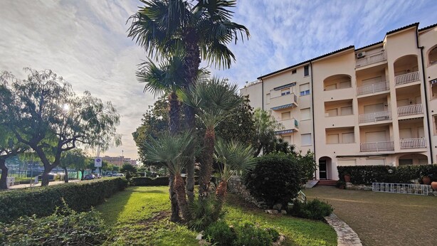 Une cour intérieure agrémentée de palmiers, une allée dallée et un immeuble à plusieurs étages doté de balcons.