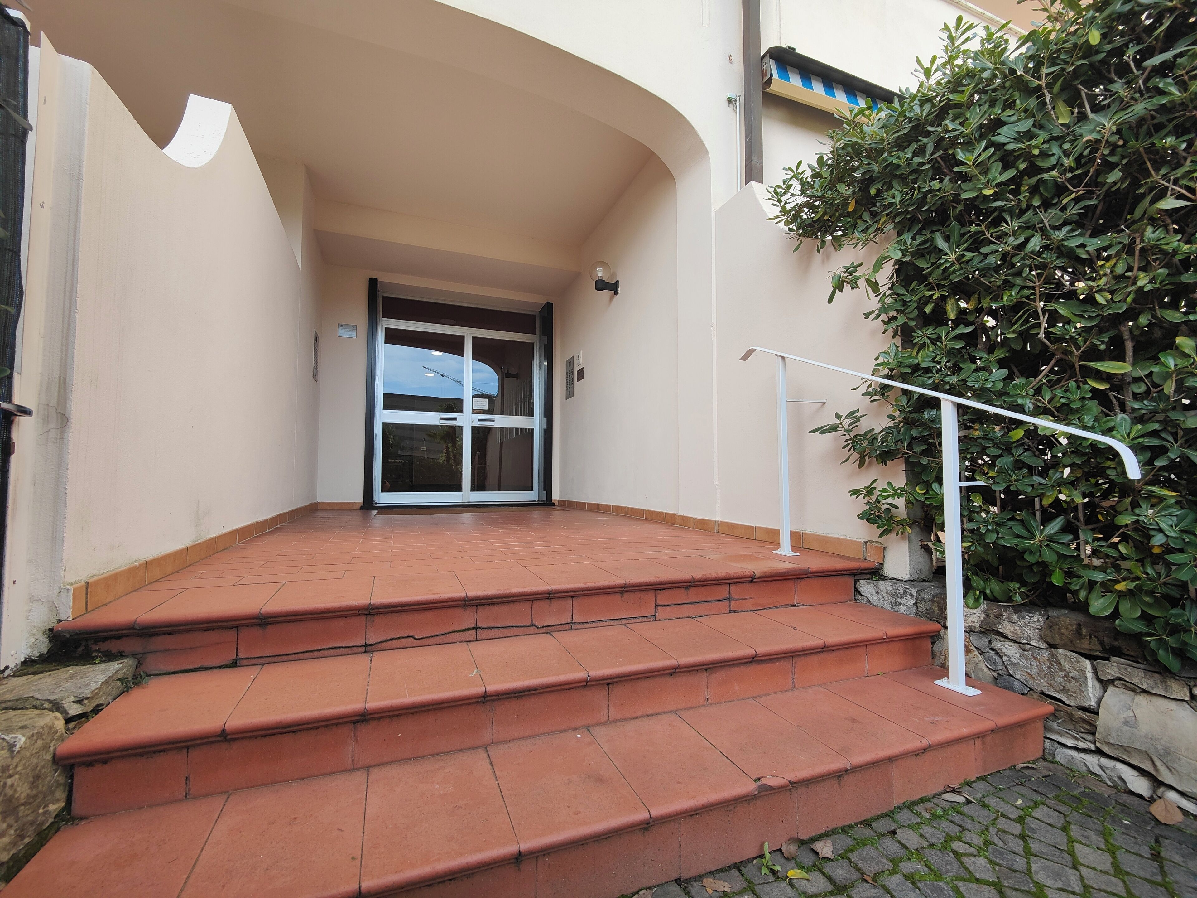 Un conjunto de escalones exteriores que llevan a la entrada de un edificio, con una puerta de cristal y barandilla blanca.