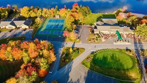 An aerial view of a golf course with a tennis court, surrounded by autumn-colored trees and a body of water. - Rustic Poconos Ranch w/ Game Room & Hot Tub (Coolbaugh Township)