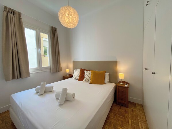 Ein Hotelzimmer mit einem großen Bett, zwei Nachttischen, einer Pendelleuchte und einem fenster mit Vorhängen.