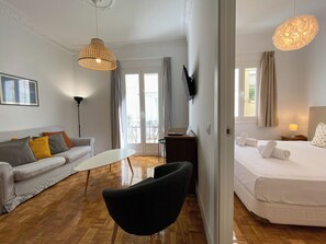 Ein modernes Hotelzimmer mit einer Sitzecke, einem kleinen Tisch, einem schwarzen Sessel, einem Bett und einem Balkon mit Vorhängen.