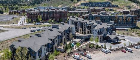 A multi-story hotel with a modern architectural design, featuring a mix of residential and commercial spaces, set against a backdrop of mountains and clear skies.