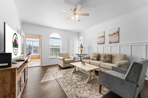 A living room with a sofa, armchair, coffee table, and a television on a wooden stand.