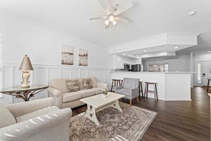 A modern living room with a sofa, coffee table, and a dining area with chairs and a kitchen in the background. - Remodeled 2BR Golf Condo • Sunroom • Sleeps 6 (Branson)
