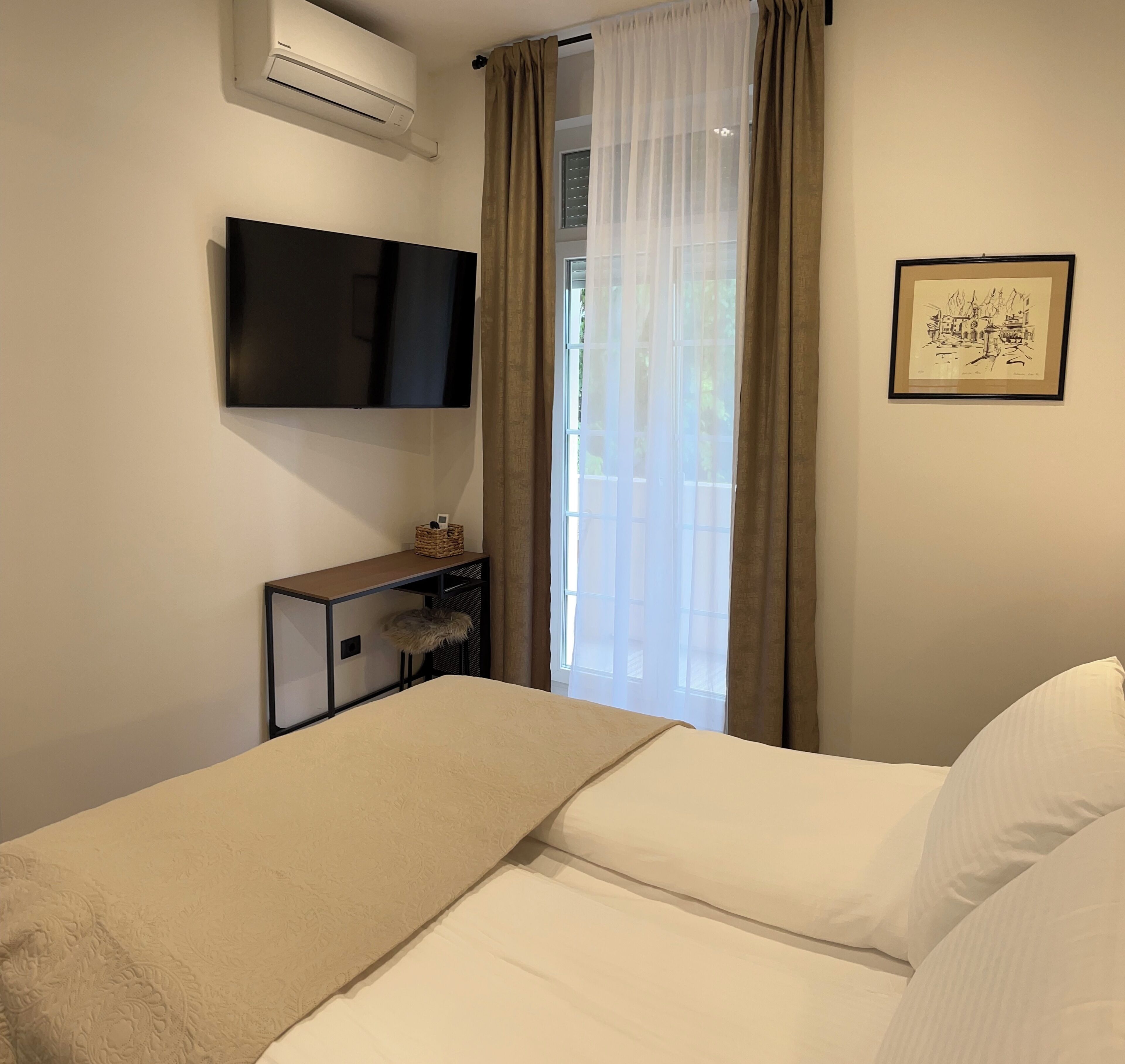 Ein Hotelzimmer mit einem Bett, einem flachbildfernseher an der Wand, einem kleinen Nachttisch mit einem Korb und einem gerahmten Bild.